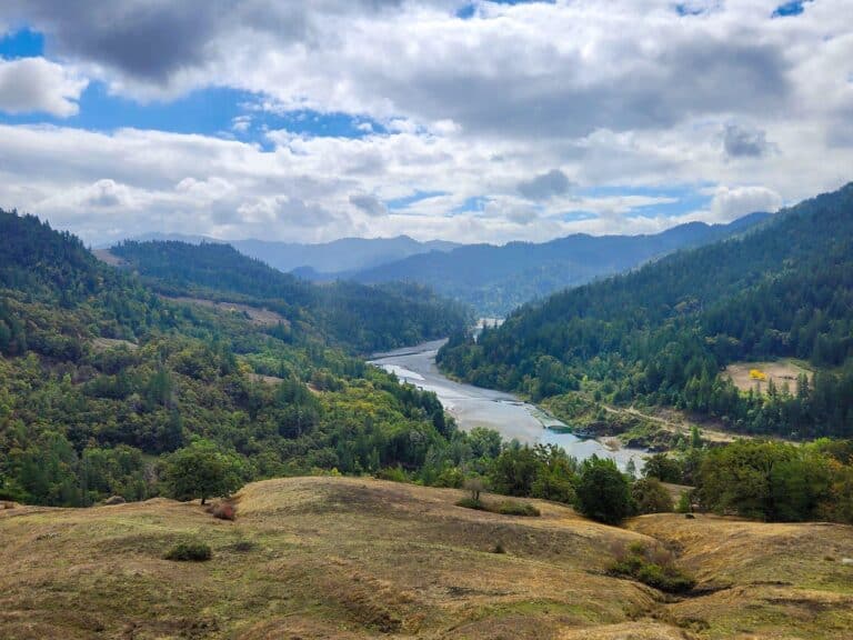 Beautiful landscape of Eel Rock Ranch with river and mountains under cloudy sky.