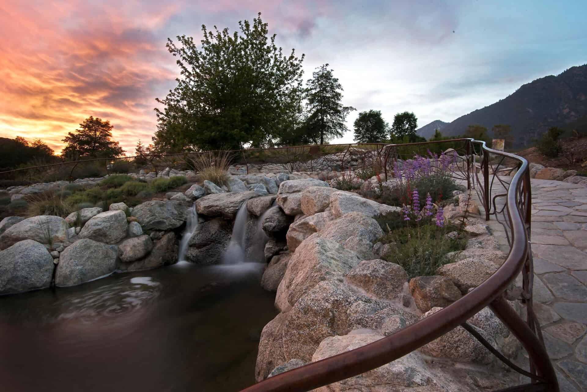 A lush natural landscape with a small waterfall and scenic mountain view at sunset.