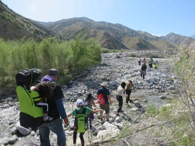 Family hiking along a rocky riverbed in scenic mountain landscape.