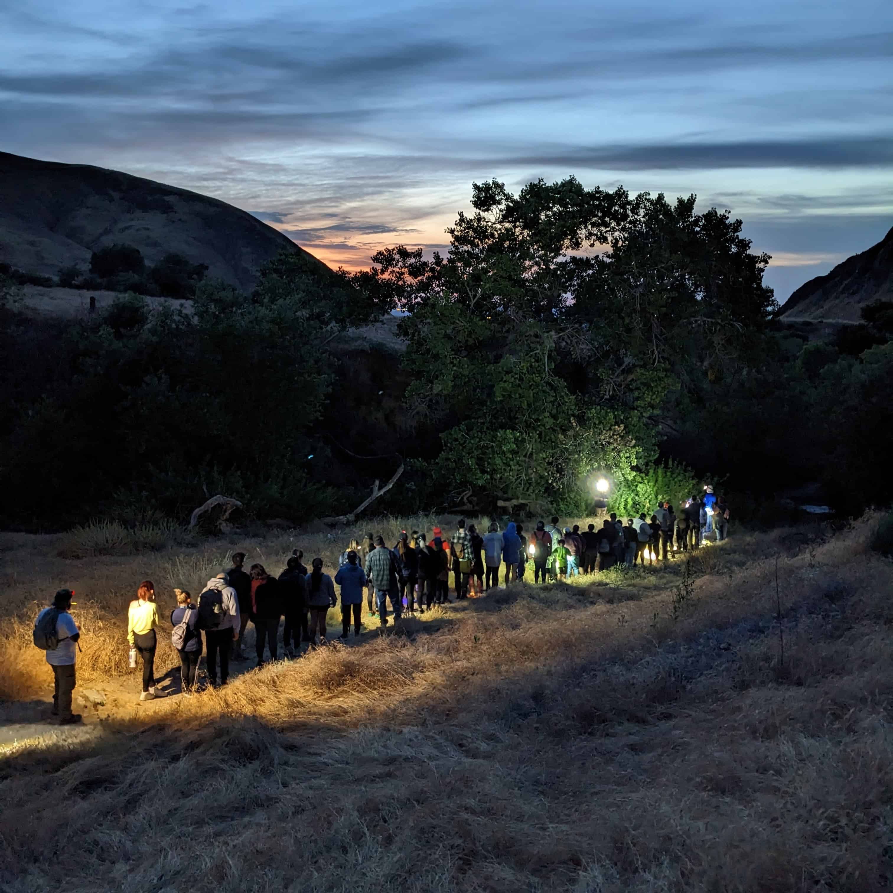 People walking along a trail during dusk in a scenic natural landscape.