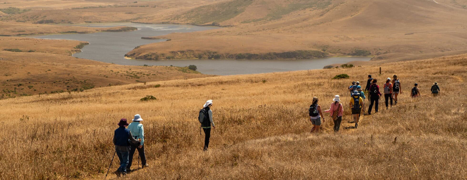 Group of hikers exploring a grassy landscape with hills and water bodies.