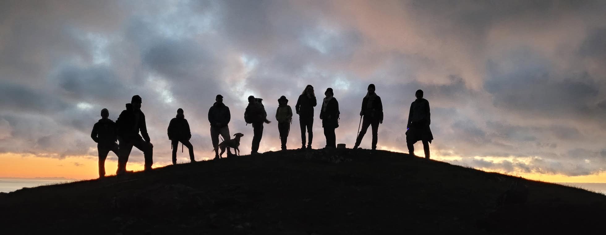 Group of hikers silhouetted against a sunset sky during a full moon hike.