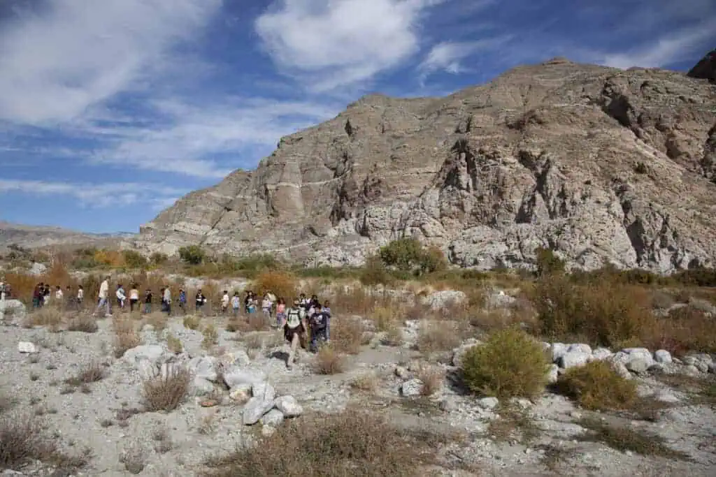 Hikers exploring a rocky desert landscape with mountains and blue sky.